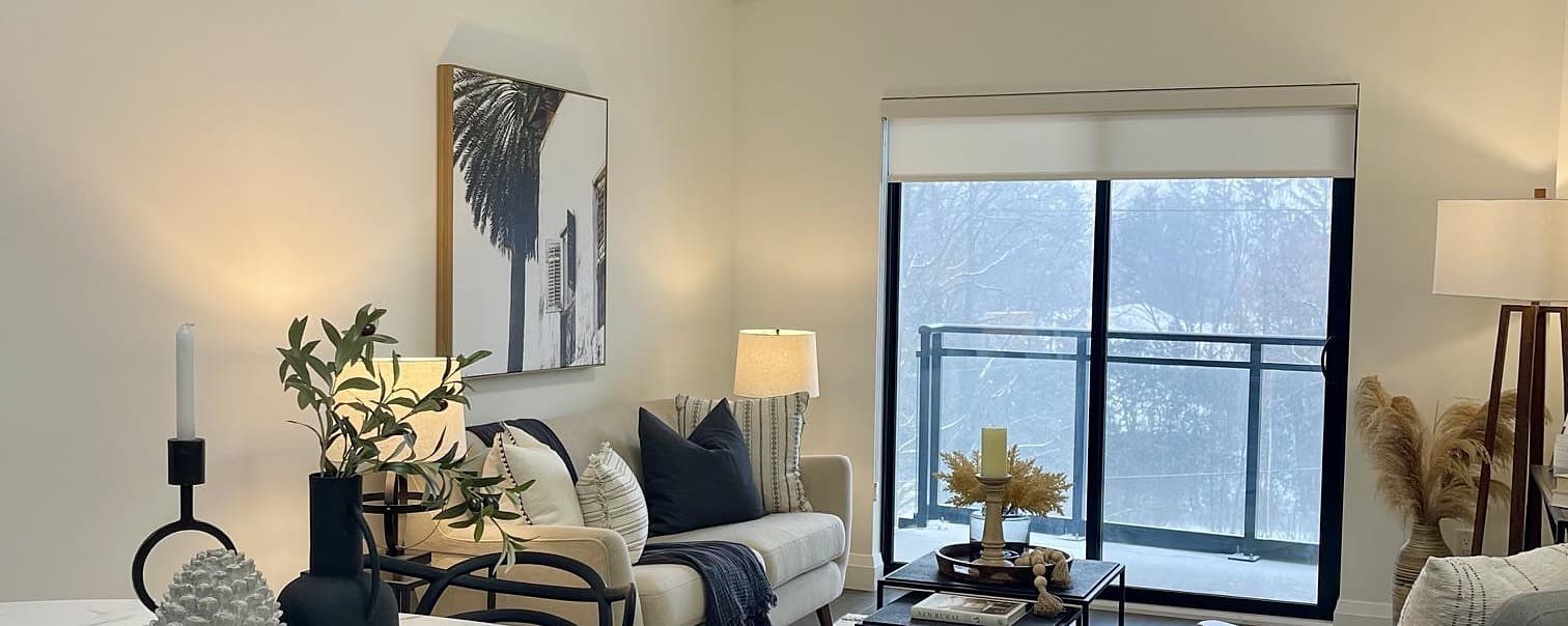 A staged condo living room with a balcony view, layered lamps, and framed art