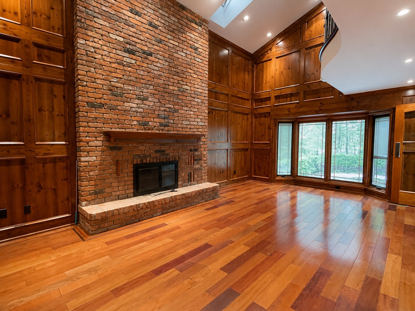 Vaulted, wood-paneled living room with a brick fireplace before staging, unfurnished
